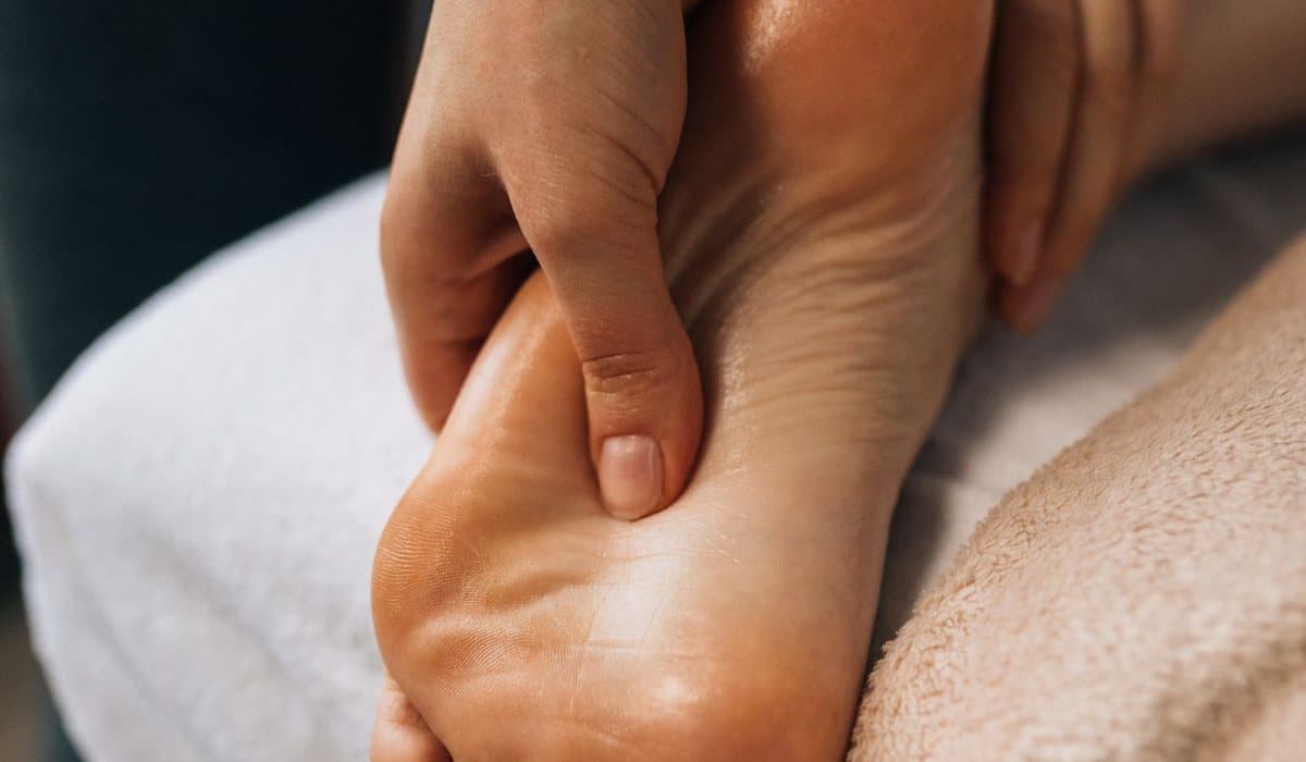Pouce du thérapeute pressant la voûte plantaire d'un pied posé sur un linge